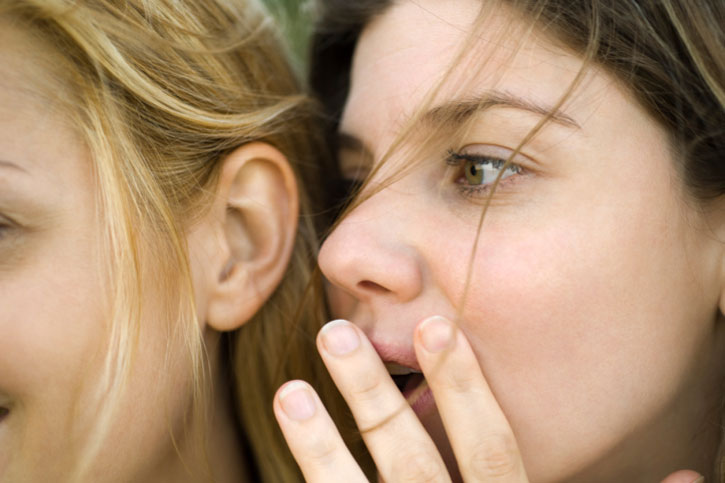 Женщина шепчет на ухо другой женщине