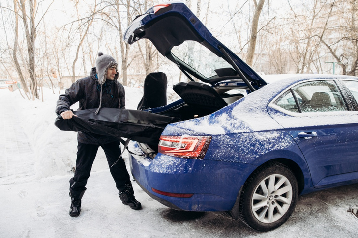 Мужчина загружает в багажник синего ŠKODA Superb лыжи в чехле